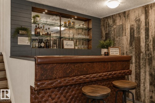 Built-in bar featuring a tufted leather front, a built-in shelving unit with glass shelves and recessed lighting, and a textured accent wall - 16016 78A Avenue Nw, Edmonton, AB 