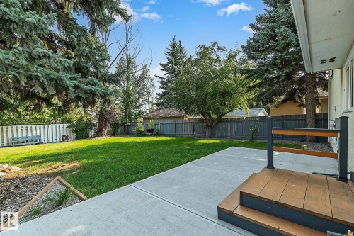 Expansive backyard featuring a concrete patio, wood-finish deck with railing, natural grass, mature trees, and perimeter fencing - 16016 78A Avenue Nw, Edmonton, AB 