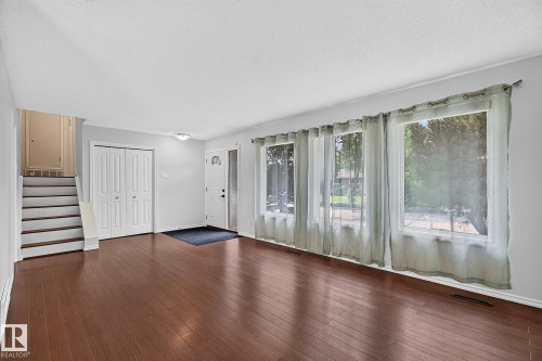 Wood-finish flooring, multiple large windows, and a classic white panel front door with a decorative glass insert - 16016 78A Avenue Nw, Edmonton, AB 