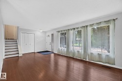 Wood-finish flooring, multiple large windows, and a classic white panel front door with a decorative glass insert - 