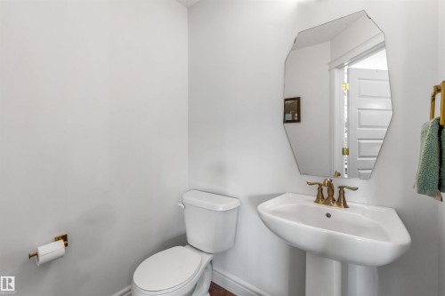 Pedestal sink with brass-finish faucet, geometric wall mirror, and white toilet - #71 330 Bulyea Rd Nw, Edmonton, AB 