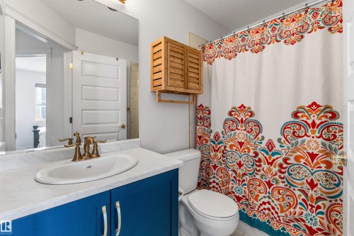 Vanity with a white countertop and blue cabinetry, brass-finish faucet, and a wall-mounted mirror - #71 330 Bulyea Rd Nw, Edmonton, AB 