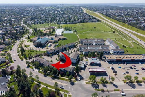 Aerial perspective of a multi-unit property with mature trees, a paved parking area, and a surrounding neighborhood featuring green spaces and infrastructure - #71 330 Bulyea Rd Nw, Edmonton, AB 