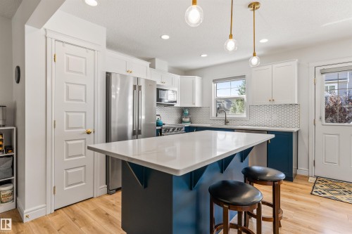 Kitchen featuring a central island with a light-toned countertop, two-toned cabinetry with brass-toned hardware, stainless steel appliances, and wood-finish flooring - #71 330 Bulyea Rd Nw, Edmonton, AB 