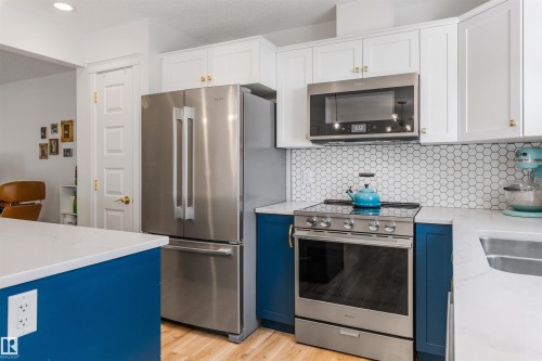 White upper cabinetry, deep blue lower cabinetry, stainless steel appliances, honeycomb tile backsplash, and light wood-finish flooring - #71 330 Bulyea Rd Nw, Edmonton, AB 