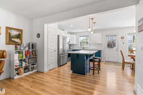 Wood-finish flooring throughout, kitchen featuring a two-toned island with seating, stainless steel appliances, and a tiled backsplash - #71 330 Bulyea Rd Nw, Edmonton, AB 