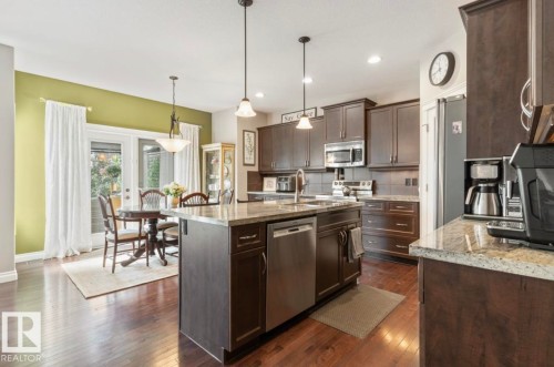 Kitchen featuring wood-finish flooring, dark wood cabinetry, stainless steel appliances, a center island with a granite-style countertop, and recessed lighting - 22 Voleta Crest, Spruce Grove, AB 