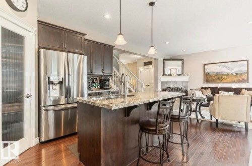 Kitchen with granite island, stainless steel refrigerator, dark wood cabinetry, and wood-finish flooring - 22 Voleta Crest, Spruce Grove, AB 