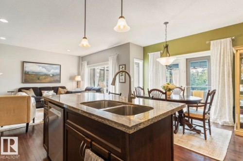 Kitchen island with dual basin sink and stone countertop, illuminated by pendant lighting - 22 Voleta Crest, Spruce Grove, AB 