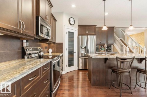 Wood-finish flooring, stainless steel appliances, granite countertops, dark wood cabinetry, and a kitchen island with pendant lighting - 22 Voleta Crest, Spruce Grove, AB 