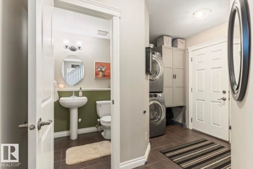 Pedestal sink, wall-mounted light fixture, tile flooring, built-in storage cabinetry, and stacked laundry appliances - 22 Voleta Crest, Spruce Grove, AB 