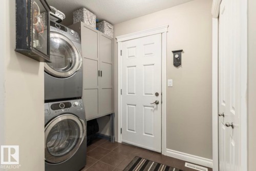 Laundry area featuring stacked appliances, built-in cabinetry, and tile flooring - 22 Voleta Crest, Spruce Grove, AB 