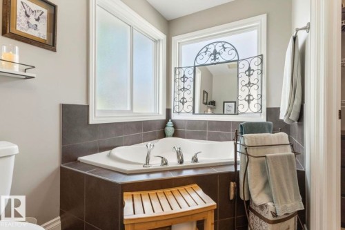Corner soaking tub with tile surround, two white-framed windows, and an ornate wall-mounted mirror - 22 Voleta Crest, Spruce Grove, AB 