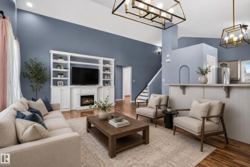 Vaulted ceilings, wood-finish flooring, built-in media center with fireplace, staircase with white risers, and decorative arched wall niche - 13803 130A Avenue Nw, Edmonton, AB 