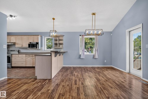 Wood-finish flooring throughout, vaulted ceiling, kitchen featuring light wood cabinetry, stainless steel appliances, and a breakfast bar - 13803 130A Avenue Nw, Edmonton, AB 