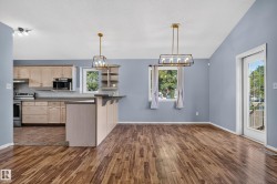 Wood-finish flooring throughout, vaulted ceiling, kitchen featuring light wood cabinetry, stainless steel appliances, and a breakfast bar - 