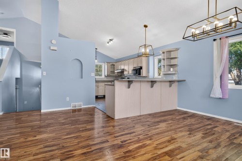 Vaulted ceilings with recessed lighting, wood-finish flooring, kitchen island with integrated shelving, and bronze-finish light fixtures - 13803 130A Avenue Nw, Edmonton, AB 