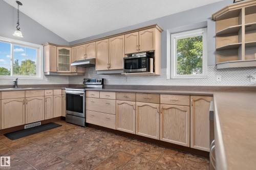 Kitchen featuring extensive wood-finish cabinetry, stainless steel appliances, a herringbone tile backsplash, and a vaulted ceiling - 13803 130A Avenue Nw, Edmonton, AB 