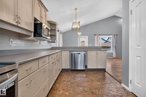 Kitchen featuring stainless steel appliances, herringbone tile backsplash, extensive cabinetry, and a vaulted ceiling - 13803 130A Avenue Nw, Edmonton, AB 