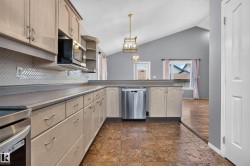 Kitchen featuring stainless steel appliances, herringbone tile backsplash, extensive cabinetry, and a vaulted ceiling - 