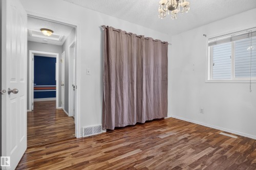 Wood-finish flooring throughout, bright window with blinds, and an overhead chandelier light fixture - 13803 130A Avenue Nw, Edmonton, AB 
