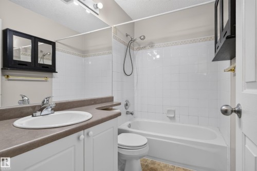 White tiled shower/tub combination, vanity with integrated sink, white cabinetry, and wall-mounted storage - 13803 130A Avenue Nw, Edmonton, AB 
