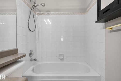 White tiled shower and bathtub combination with a decorative tile border, featuring a chrome shower head and faucet - 13803 130A Avenue Nw, Edmonton, AB 