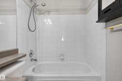 White tiled shower and bathtub combination with a decorative tile border, featuring a chrome shower head and faucet - 