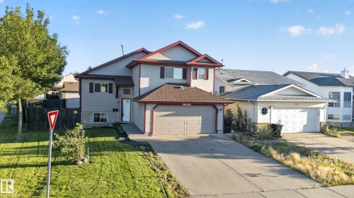 Two-story residence featuring light gray siding with dark trim accents, an attached garage, a paved driveway, and a front yard with manicured lawn - 13803 130A Avenue Nw, Edmonton, AB 