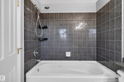 White soaking tub with integrated jets, dark gray tile surround, decorative tile accent band, and chrome shower fixtures - 