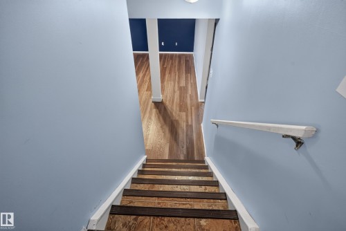 Staircase with wood-finish treads and risers, light blue painted walls, and a white handrail - 13803 130A Avenue Nw, Edmonton, AB 