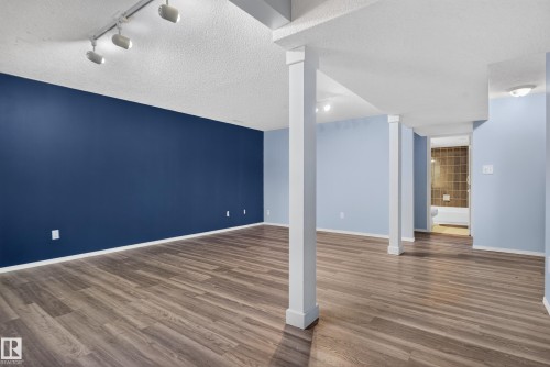 Spacious room featuring wood-finish flooring, a track lighting system, and a distinct accent wall - 13803 130A Avenue Nw, Edmonton, AB 