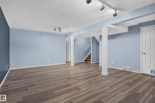 Expansive room featuring wood-finish flooring, light blue walls, exposed structural beams, white trim, and track lighting - 13803 130A Avenue Nw, Edmonton, AB 