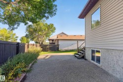 Siding exterior with multiple windows, leading to a fenced yard with mature trees and a gravel surface - 