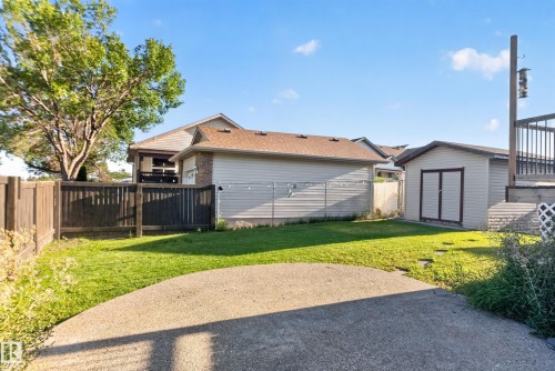 Expansive backyard featuring a concrete patio, manicured lawn, wood fencing, and a detached storage shed - 13803 130A Avenue Nw, Edmonton, AB 