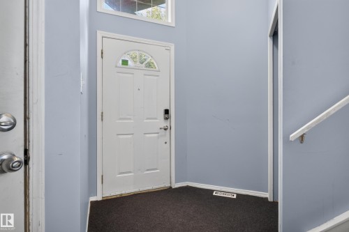 Entryway featuring a white paneled door with an arched glass insert, smart lock hardware, upper transom window, and carpeted flooring - 13803 130A Avenue Nw, Edmonton, AB 