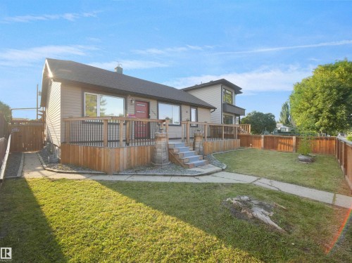 Siding exterior with a red entry door, elevated wood deck with black railings, and a fenced yard - 13338 131 Street Nw, Edmonton, AB 
