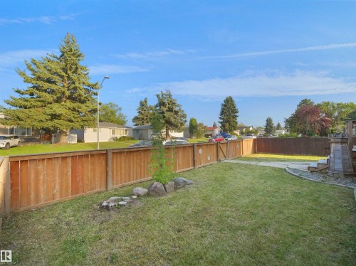 Expansive green lawn with a wood plank fence, bordered by decorative rocks and a small tree - 13338 131 Street Nw, Edmonton, AB 