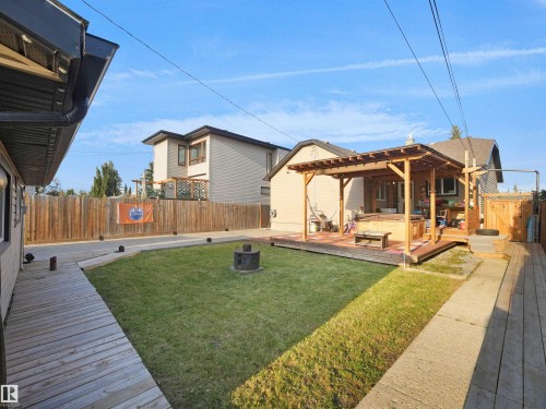 Expansive backyard featuring a manicured lawn, a wooden deck with a pergola, a fire pit, and privacy fencing - 13338 131 Street Nw, Edmonton, AB 