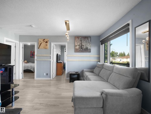 Wood-finish flooring throughout, light blue wall paint, and a large window with roller shades - 13338 131 Street Nw, Edmonton, AB 