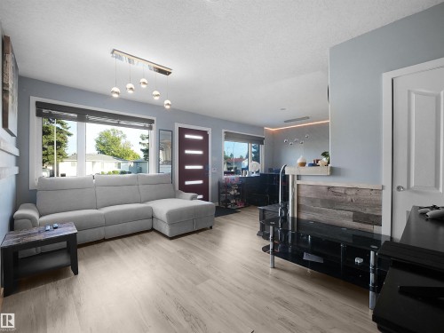 Light wood-finish flooring, a contemporary chandelier, two large windows, and a modern red entry door - 13338 131 Street Nw, Edmonton, AB 
