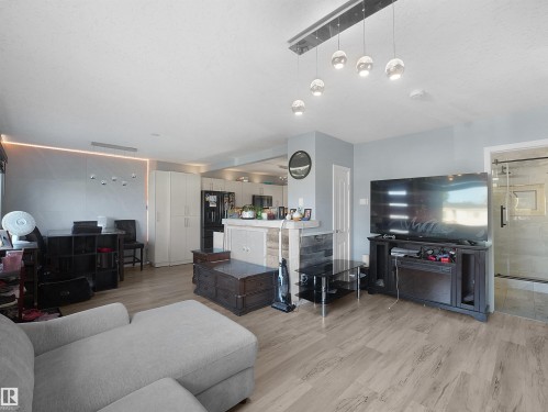 Open-concept living area featuring wood-finish flooring, a contemporary linear pendant light fixture, and a sliding glass barn door - 13338 131 Street Nw, Edmonton, AB 