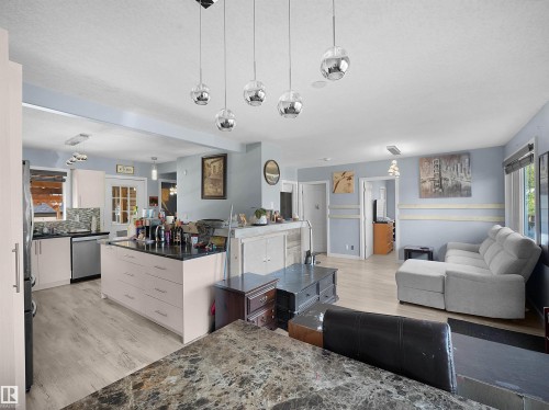 Open-concept living area featuring a kitchen island with dark countertop, light wood-finish flooring, recessed lighting, and modern pendant light fixtures - 13338 131 Street Nw, Edmonton, AB 
