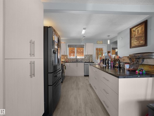 Light-toned full-height cabinetry, black refrigerator, wood-finish flooring, dark countertop, and mosaic tile backsplash - 13338 131 Street Nw, Edmonton, AB 
