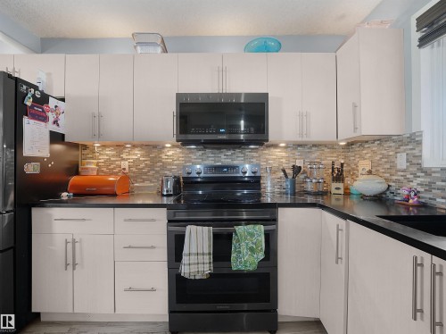 White flat-panel cabinetry, black countertops, and a full-height tile backsplash - 13338 131 Street Nw, Edmonton, AB 