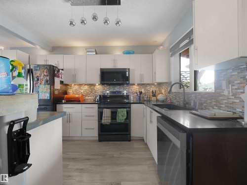 Kitchen featuring wood-finish flooring, white cabinetry, a tile backsplash, and dark countertops - 13338 131 Street Nw, Edmonton, AB 