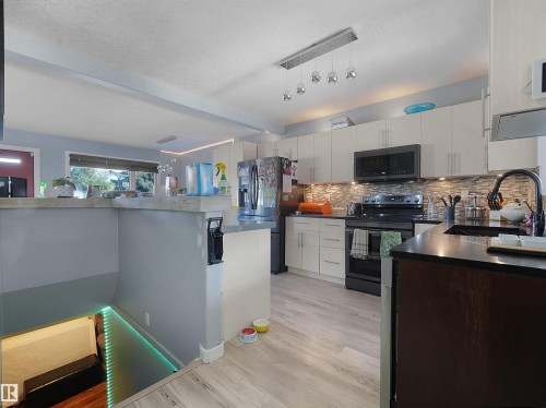 Kitchen featuring light wood-finish flooring, dark countertops, and a mosaic tile backsplash - 13338 131 Street Nw, Edmonton, AB 