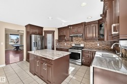 Kitchen featuring dark wood cabinetry, stainless steel appliances, light-toned tile flooring, light-toned stone countertops, and a stone-finish backsplash - 