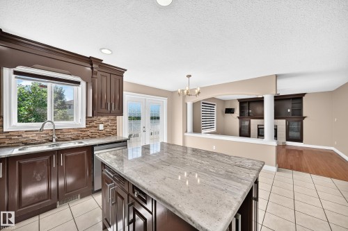 Gourmet kitchen featuring dark wood cabinetry, stone-finish countertops, and a large center island with seating - 4711 152 Avenue Nw, Edmonton, AB 