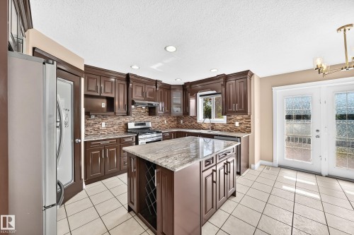 Dark wood-finish cabinetry with crown molding, stone countertops, and a tiled backsplash - 4711 152 Avenue Nw, Edmonton, AB 
